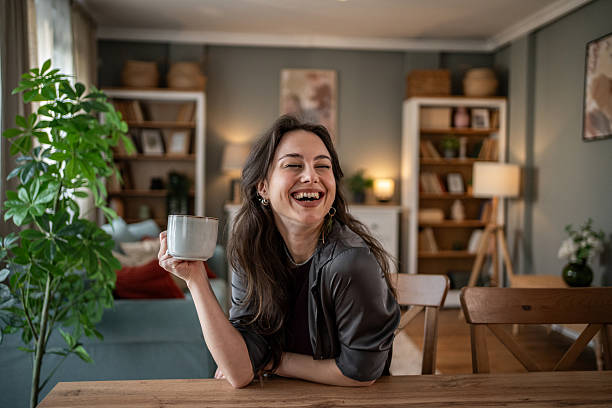 istock Young woman laughing while drinking coffee at home 2210225673