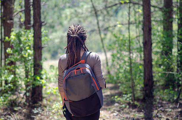 istock A young woman hikes through a lush green forest, sunlight filtering through the branches above. With her long hair flowing and a backpack on her shoulders, she takes in the energizing tranquility of nature. 2210231074