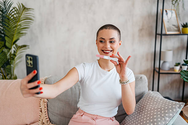 istock Happy Young Woman With A Buzz Cut Taking Selfies While Holding A Pregnancy Test She Just Took At Home 2210233401