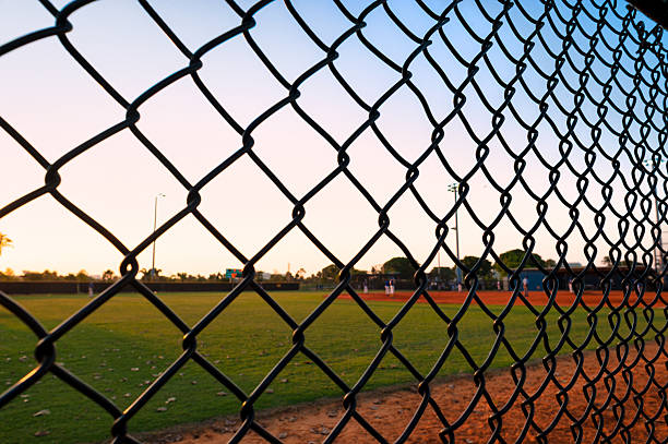 istock Evening youth league baseball game in progress viewed through chain-link fence at twilight 2210236061
