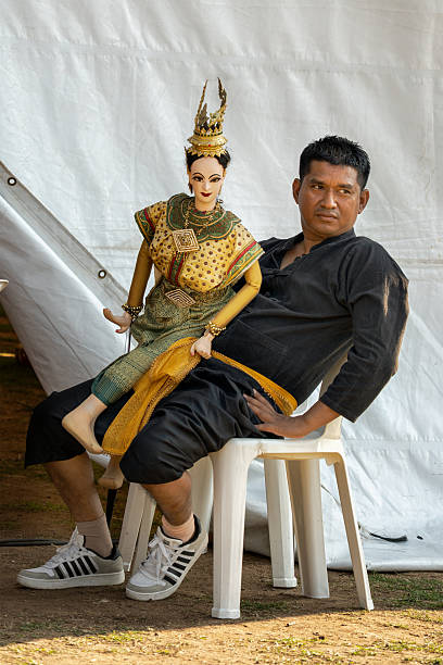 Pattaya, Thailand, Feb.15, 29025: The puppeteer dressed in black is taking a break while carrying his elaborate puppet dressed in a stunning traditional outfit with gold accents and a fancy headdress.