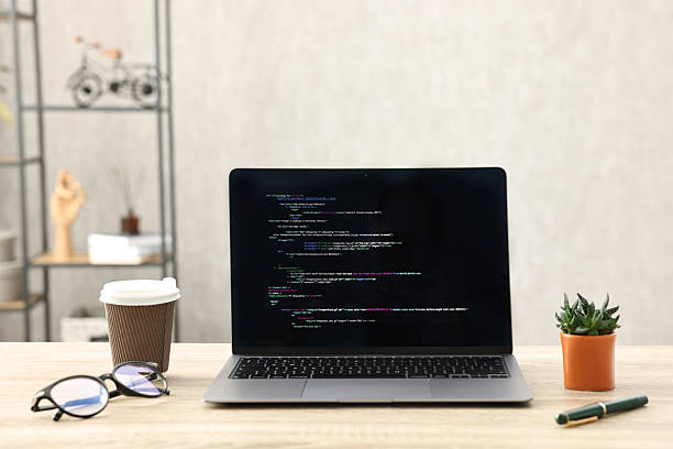 istock Programmer's workplace. Modern laptop with unfinished code, paper cup of drink, glasses and houseplant on desk indoors 2210247952