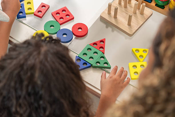 Two children building and arranging colorful wooden blocks and beads at an outdoor table, symbolizing teamwork and learning.