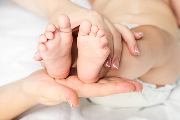 istock Newborn baby feets in mother hands on white bed 2210250814