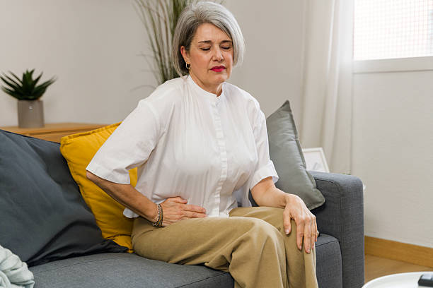 istock Senior woman suffering abdominal pain while sitting on sofa at home 2210252038