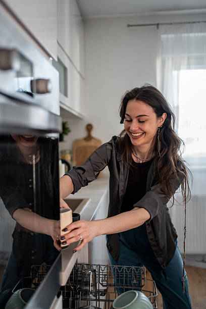 istock Young woman loading dishes into dishwasher in modern kitchen 2210252397