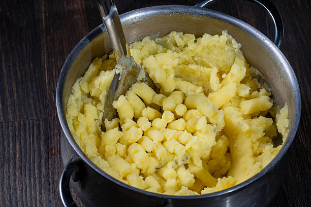 istock Fresh mashed potatoes mashed with a metal masher in a saucepan on a wooden table, closeup 2210252780
