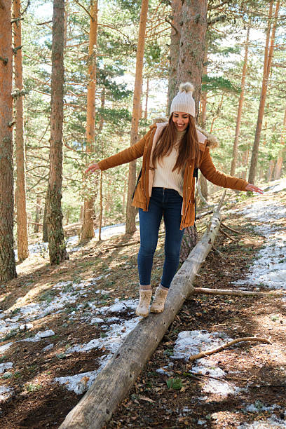 istock Young woman balancing on a log in a snowy forest during winter 2210253798
