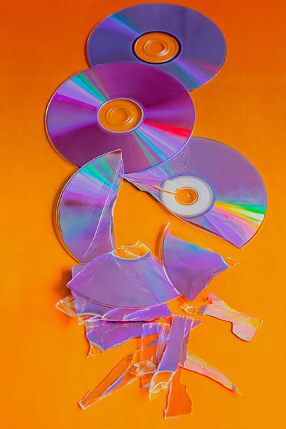 Whole and broken compact discs on an orange background, close-up shot, old vintage technology, loss and restoration of an archive.