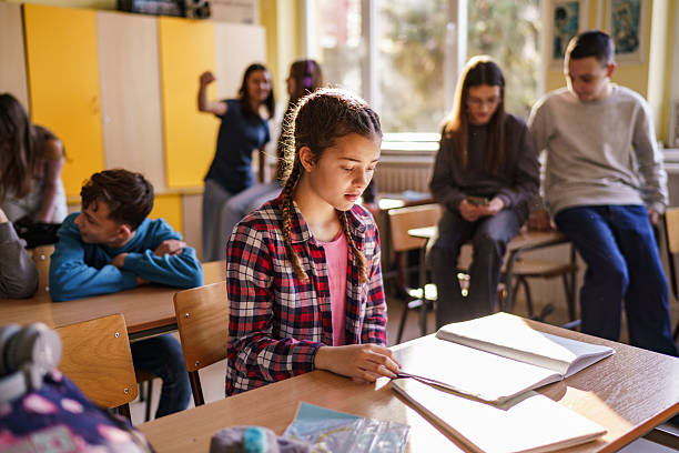 istock Girl reading a book while other students talking in the background 2210255365