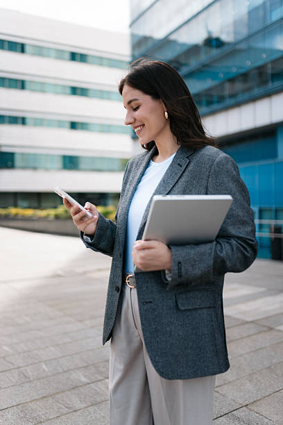 istock Smiling businesswoman using smartphone and holding tablet in urban setting 2210258091