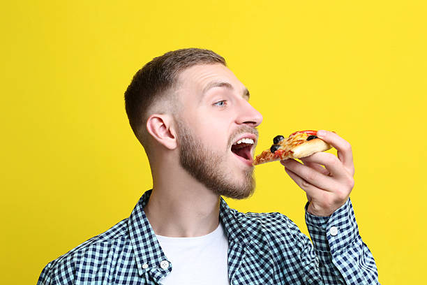 istock Young man eating pizza on yellow background 2210258227