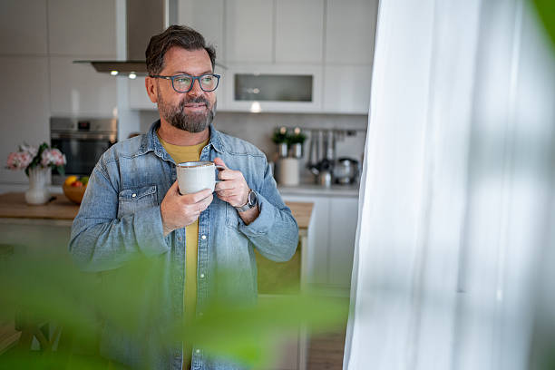 istock Smiling mature man drinking coffee and looking out the window in his modern kitchen 2210261047