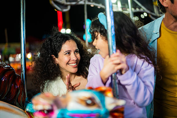 An African-American sweet girl child with afro curls and a cute Caucasian boy ride together on a carousel in an amusement park in the evening on weekend and have fun.