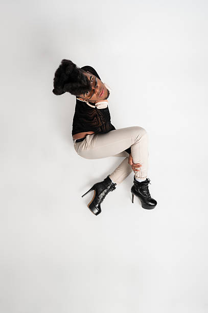 Young stylish musician sitting comfortably on the floor, wearing trendy headphones and confidently looking at the camera against a white background