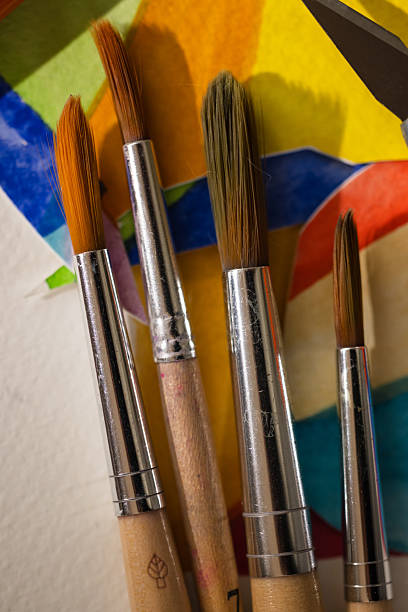 Macro close-up of paintbrush tips placed across a vibrant paper collage in primary colors. A richly detailed composition capturing creativity, craftsmanship, and art process.