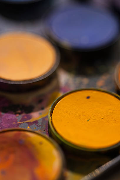 Close-up of vibrant watercolor pans in deep blue, purple, and orange tones. The paint surface is splattered with dried pigment, highlighting artistic use and dynamic contrast.