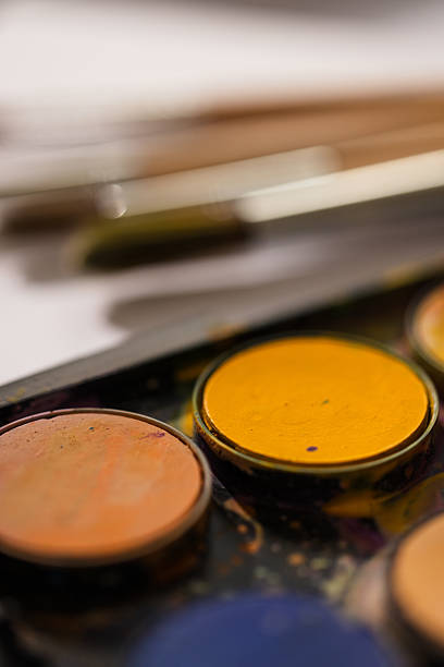 Flat lay of colorful watercolor paints and a selection of painting brushes placed on white textured paper. Clean and minimal artistic background.