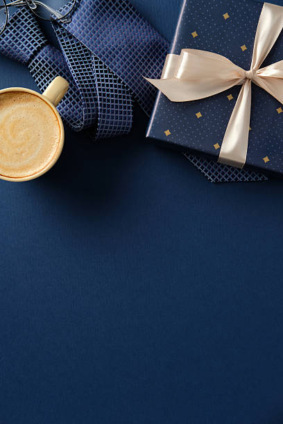 istock Flat lay Father's Day gift: tie, coffee, glasses, wrapped present on blue background. 2210270824