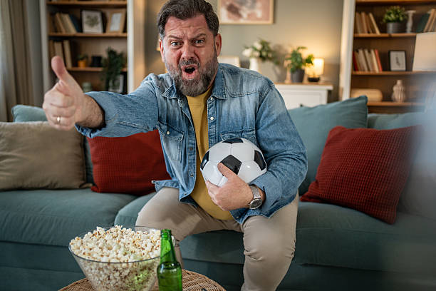 istock Excited soccer fan cheering and holding ball while watching tv 2210276343