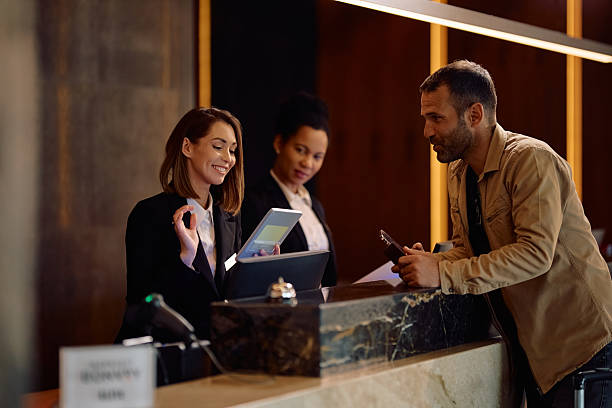 istock Happy female receptionist using touchpad while welcoming a guest in a hotel. 2210276714