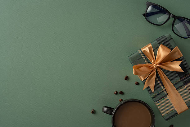 istock Gift box with ribbon, coffee cup, sunglasses, and green background evoking celebration 2210278825