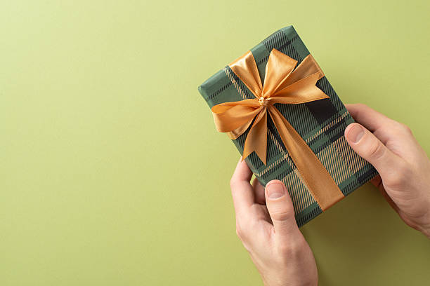 istock Hands holding a wrapped gift box featuring a plaid pattern with a golden ribbon bow 2210278827
