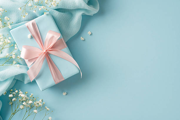 istock Charming pastel gift box adorned with a pink ribbon, surrounded by delicate flowers and fabric 2210278831