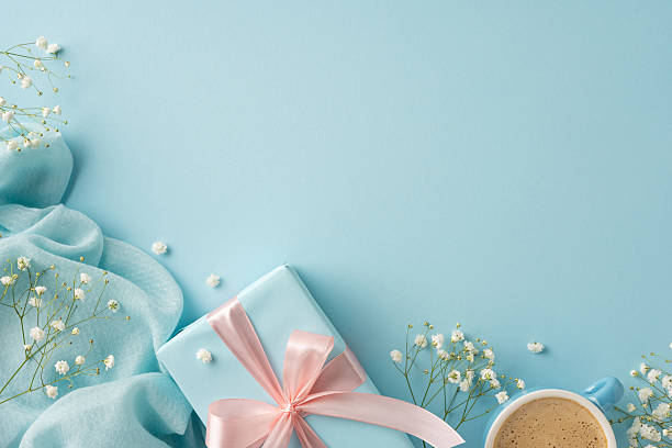 istock Stylish composition featuring a gift box with a light pink ribbon, delicate flowers, and a coffee cup on a modern blue textured surface 2210278835