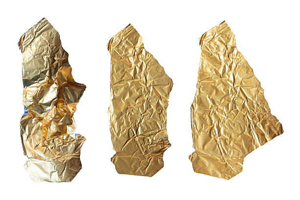 istock Three irregular pieces of crumpled golden foil displayed vertically on a plain white background. The metallic texture reflects light, creating dynamic highlights and shadows across each torn segment. 2210286856