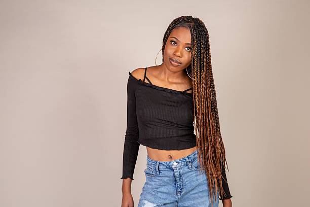 Studio shot of a young Black woman with vintage orange top and baggy jeans posing on a white background