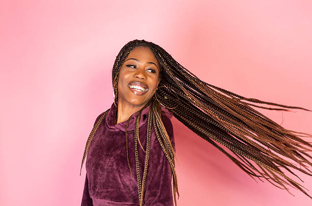 African American woman with amazing braided long hair in a casual urban lifestyle outfit on a pink backdrop