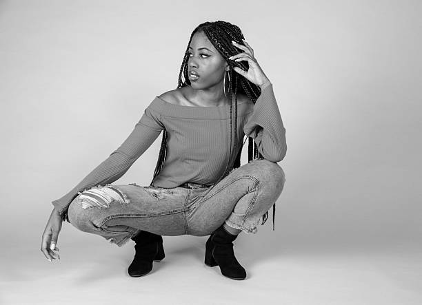 Studio shot of a young Black woman with vintage orange top and baggy jeans posing on a white background