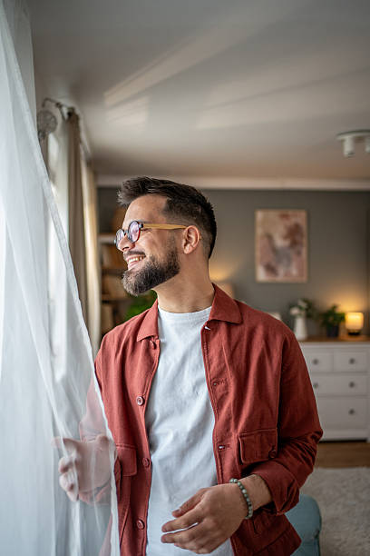 istock Young man smiling and looking out the window at home 2210289791