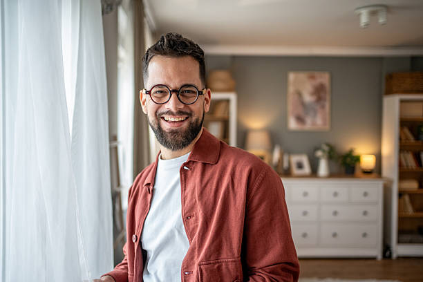 istock Young man smiling near window at home 2210289816