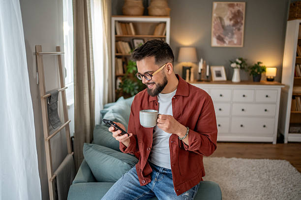 istock Young man relaxing on sofa, enjoying coffee and browsing smartphone at home 2210289888