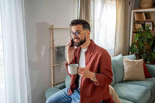 istock Young man relaxing on sofa, enjoying coffee and phone call at home 2210289891