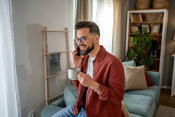 istock Young man relaxing on sofa, enjoying coffee and phone conversation at home 2210289892