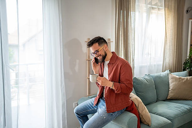 istock Young man relaxing on sofa, drinking coffee and talking on phone 2210289903