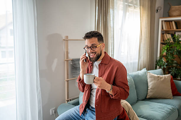 istock Young man talking on the phone and drinking coffee at home 2210289908