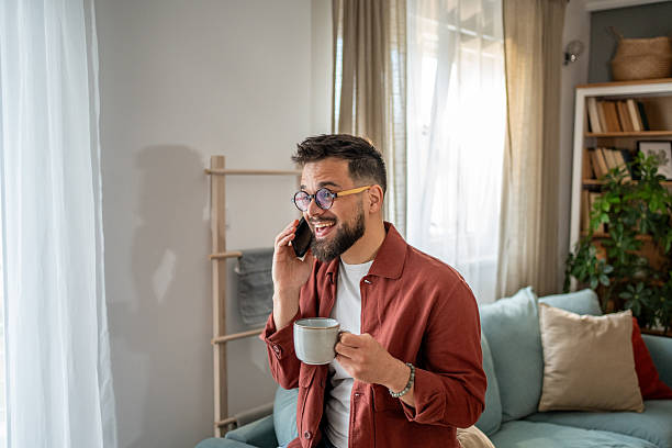 istock Young man talking on the phone and drinking coffee at home 2210289909