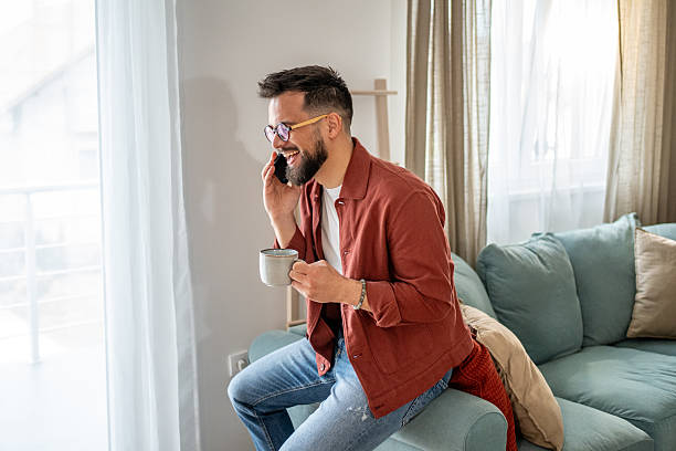 istock Young man talking on the phone and drinking coffee at home 2210289920