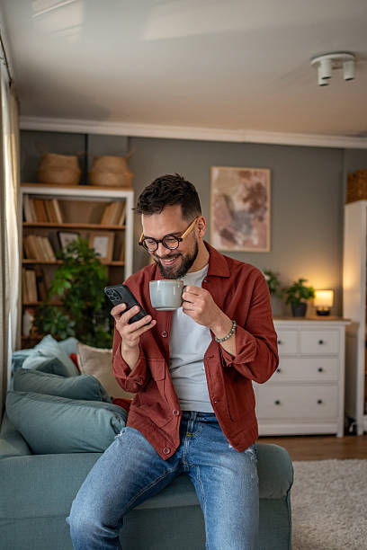istock Young man relaxing on sofa, enjoying coffee and browsing smartphone at home 2210289932