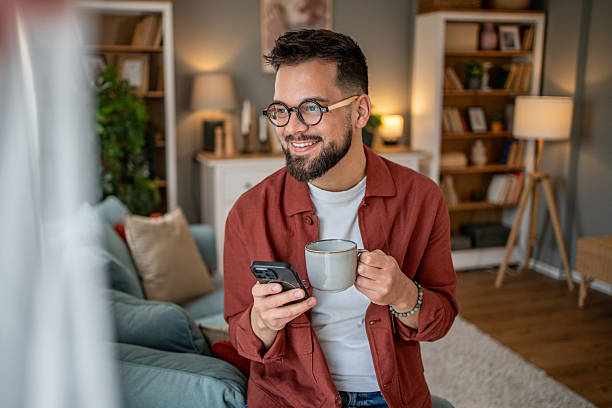 istock Young man relaxing on sofa, enjoying coffee and browsing smartphone at home 2210290448