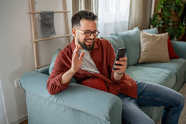 istock Happy man waving hand while video calling on smartphone at home 2210290471