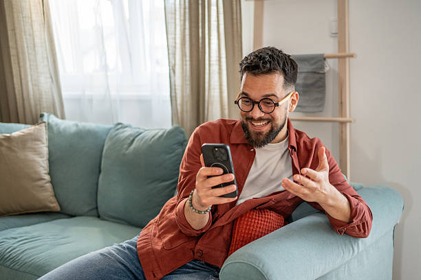 istock Young man video calling with friends while relaxing on sofa at home 2210290472