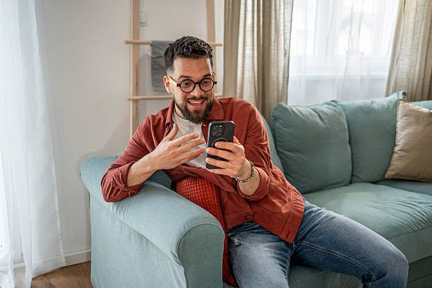 istock Young man video calling with smartphone at home on sofa 2210290481