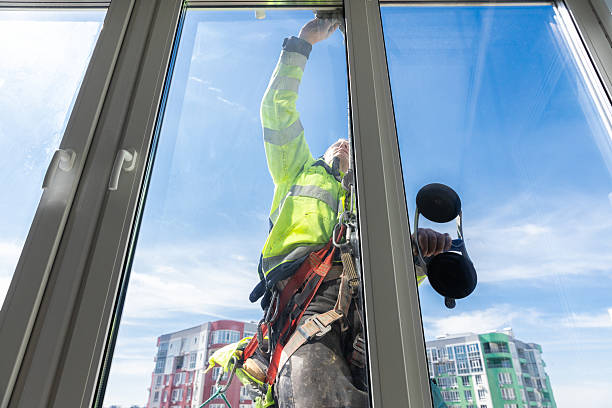 istock Professional Window Cleaner in a Safety Harness Performing Duties on a High Rise Building with a Blue Sky in the Background, Showcasing the Importance of Safety in Construction 2210290670