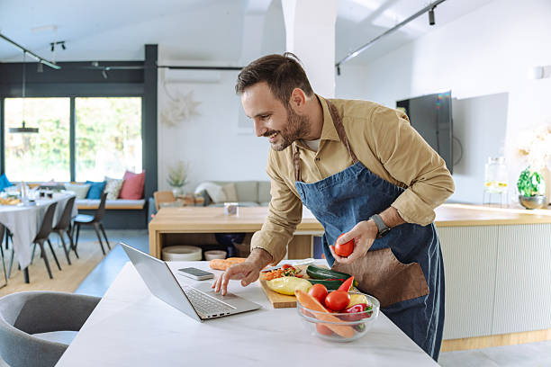 istock Man cooking in kitchen using a laptop for recipe guidance and preparation 2210293863