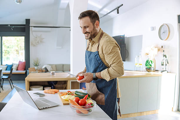 istock Man cooking vegetables at home using a laptop in a modern kitchen 2210293881
